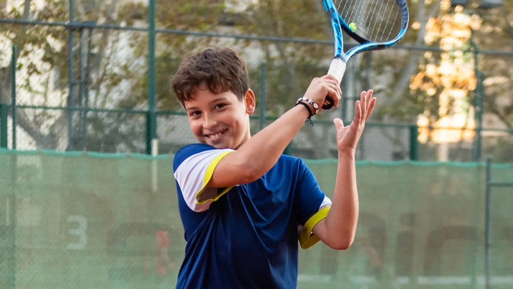 nen jugant a tenis a la pista de terra batuda del CEM Olímpia